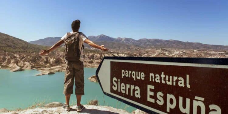 Hombre con mochila contemplando el paisaje en el Parque Natural Sierra Espuña, con un cartel señalando el lugar.