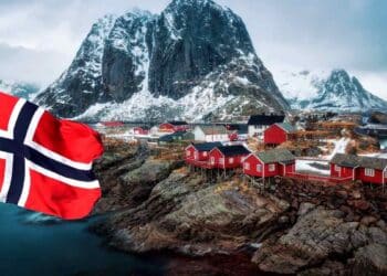 Paisaje de Noruega con casas rojas y bandera noruega ondeando, relacionado con oportunidades de trabajo en piscifactorías de salmón.