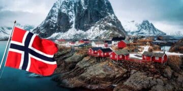 Paisaje de Noruega con casas rojas y bandera noruega ondeando, relacionado con oportunidades de trabajo en piscifactorías de salmón.