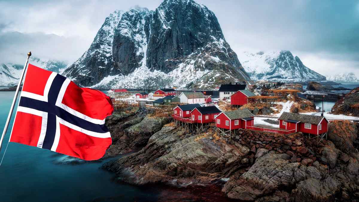 Paisaje de Noruega con casas rojas y bandera noruega ondeando, relacionado con oportunidades de trabajo en piscifactorías de salmón.