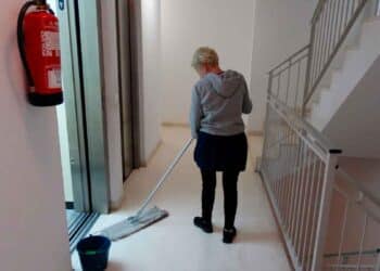 Mujer limpiando un pasillo en una comunidad de vecinos con un mocho y cubo de agua.