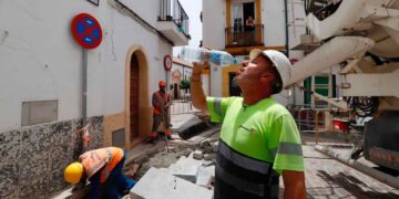 Obreros en una obra urbana, con uno de ellos bebiendo agua bajo el calor. Imagen representativa del sector de la construcción y las ofertas de empleo de Elecnor.