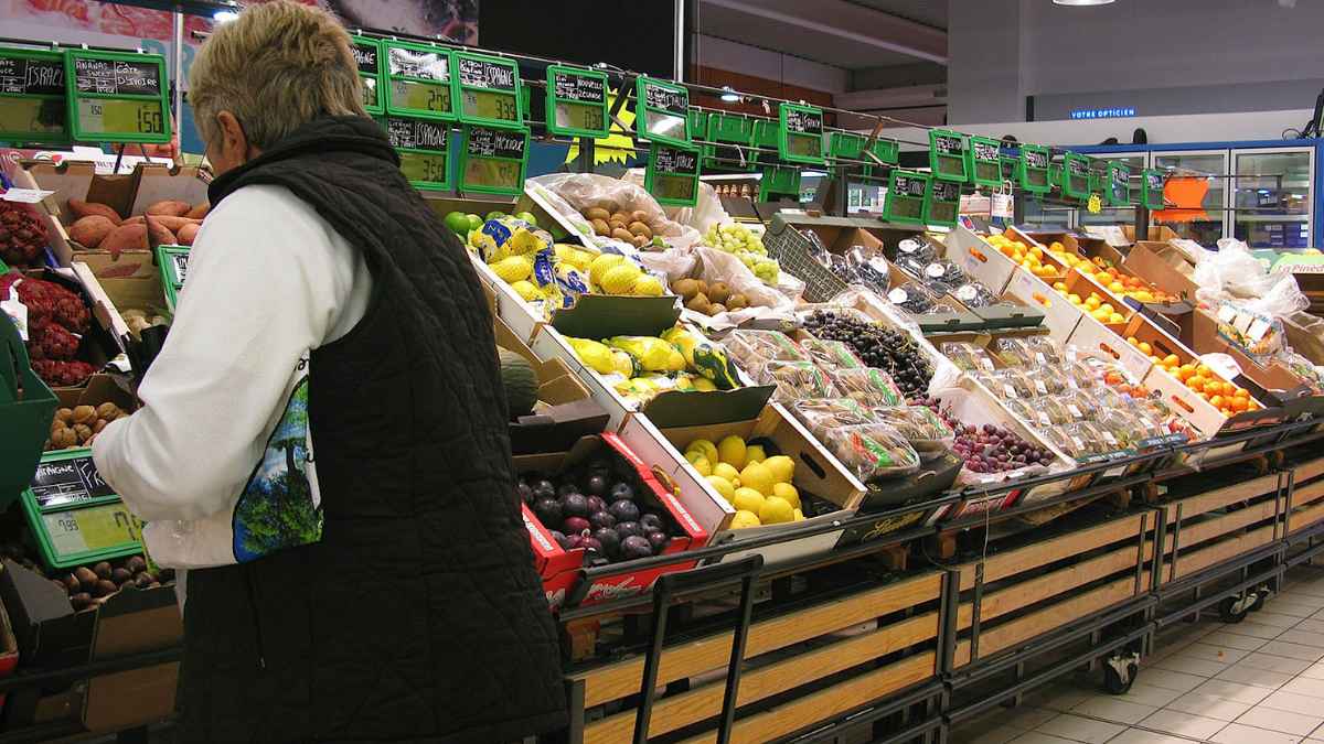 Mujer comprando frutas y verduras en un supermercado, ilustrando el contexto de cierres de Intermarché