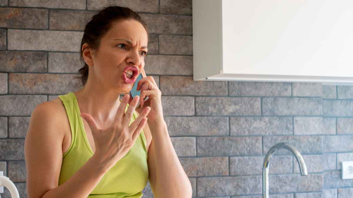 Mujer enfadada hablando por teléfono en la cocina, ilustrando el conflicto por la pensión de 350 euros