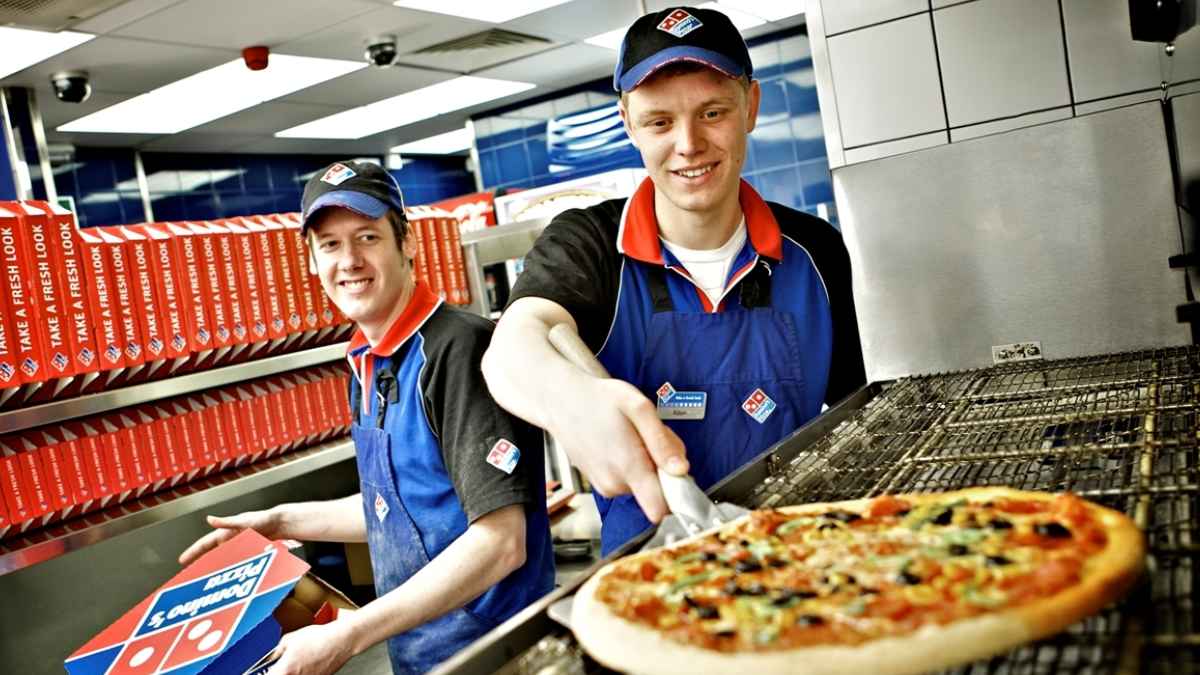 Dos empleados de Domino's Pizza sacan una pizza del horno y preparan cajas en la tienda