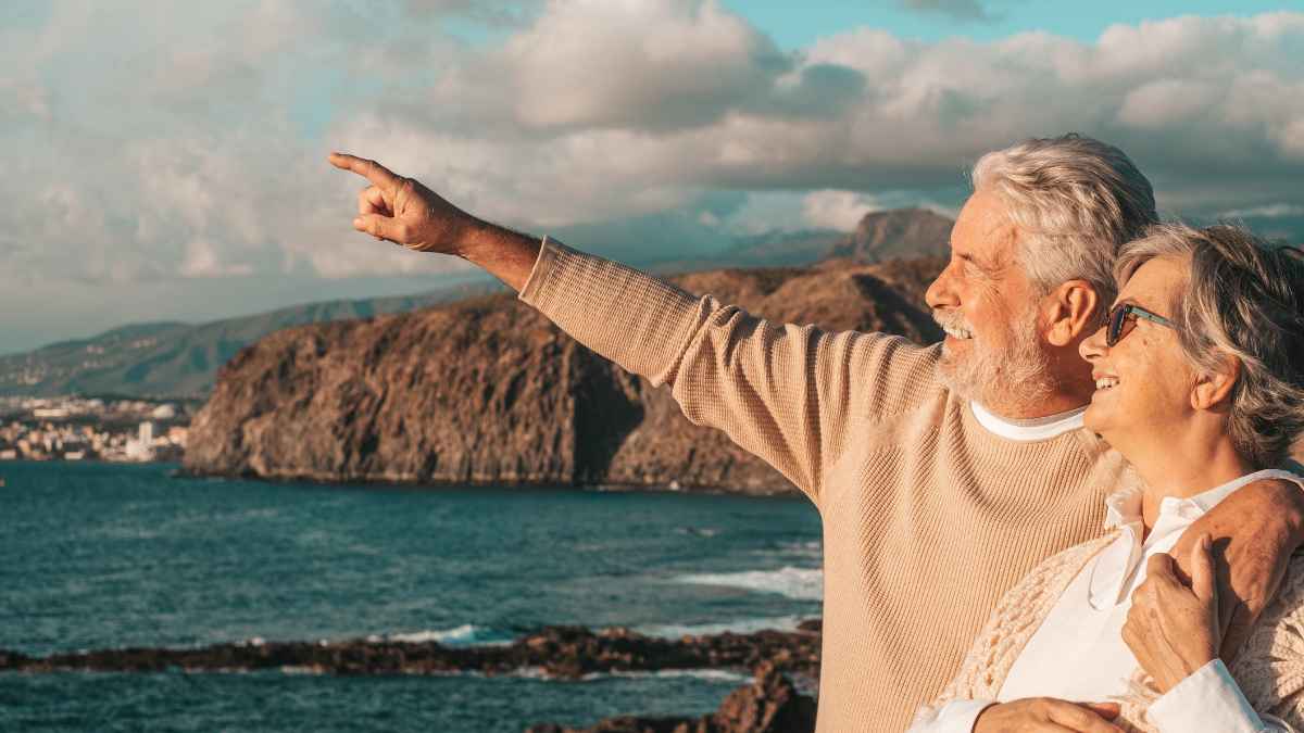 Pareja de jubilados sonrientes señala el horizonte desde un crucero mientras explica cómo ahorrar la pensión