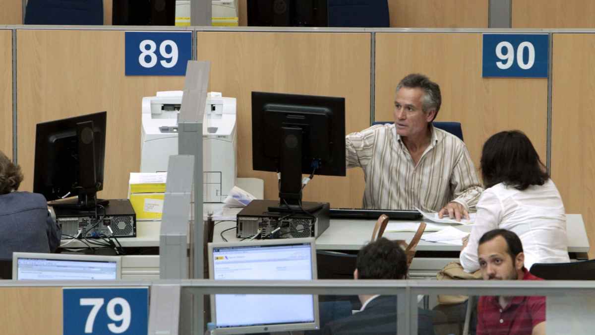 Funcionario atiende a una ciudadana en un mostrador de la Administración mientras sigue pendiente la subida salarial del 0,5 % reclamada por los sindicatos