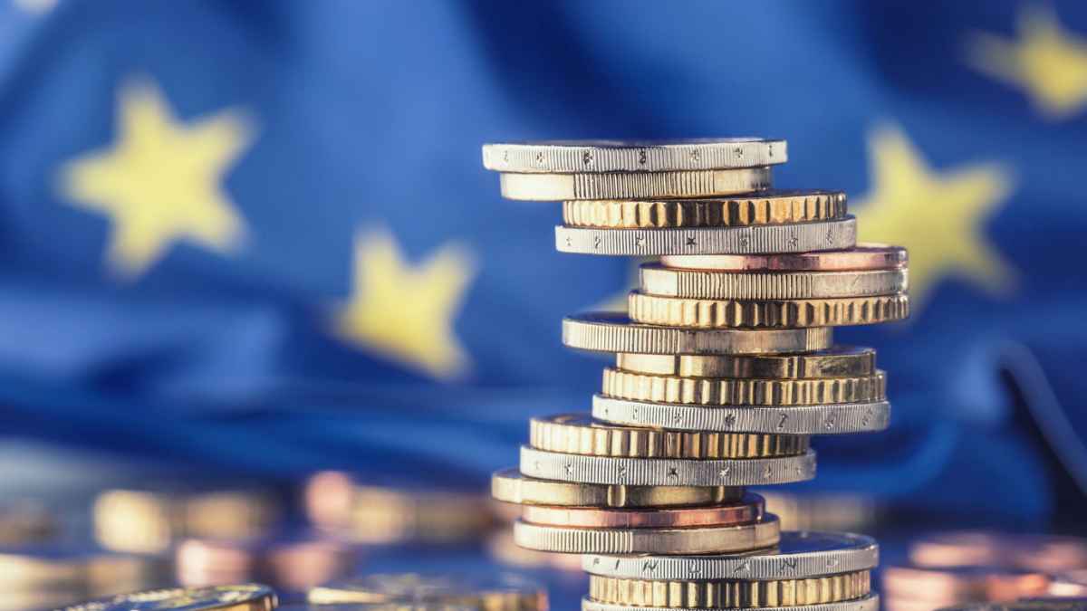 Monedas de euro apiladas frente a la bandera de la Unión Europea simbolizan el nuevo límite de 10.000 euros en efectivo