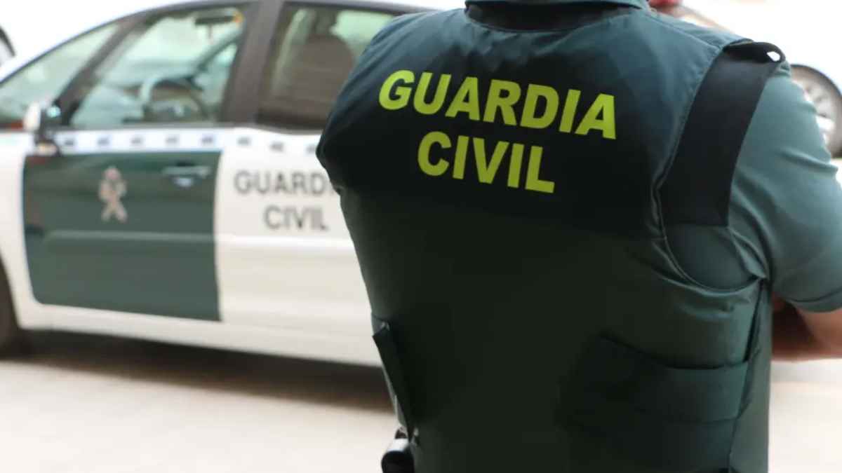 Agente de la Guardia Civil junto a un coche patrulla, ilustrando la alerta de estafa telefónica con prefijos +355, +225, +233 y +234