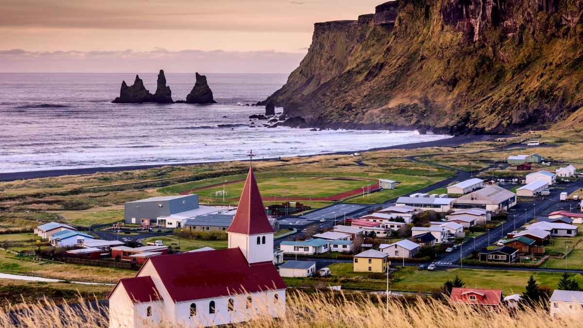 Vista panorámica de un pueblo costero en Islandia al atardecer con acantilados y formaciones rocosas marinas.