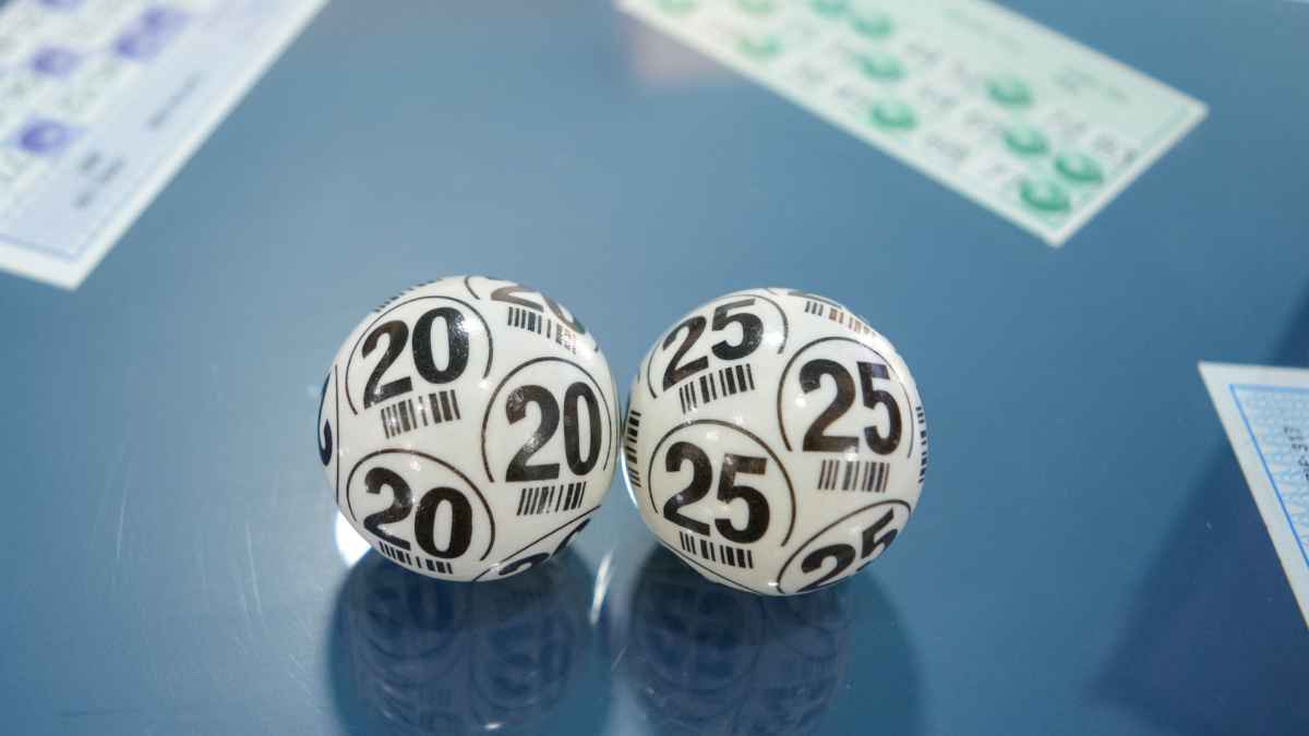 Bolas de lotería con los números 20 y 25 sobre una mesa azul junto a varios boletos.