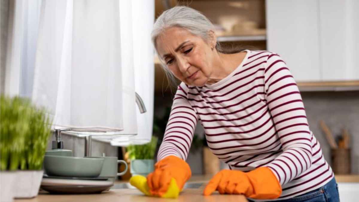 Mujer sénior limpiando la encimera con guantes, símbolo de las amas de casa que podrán cobrar la pensión de 500 euros del Gobierno