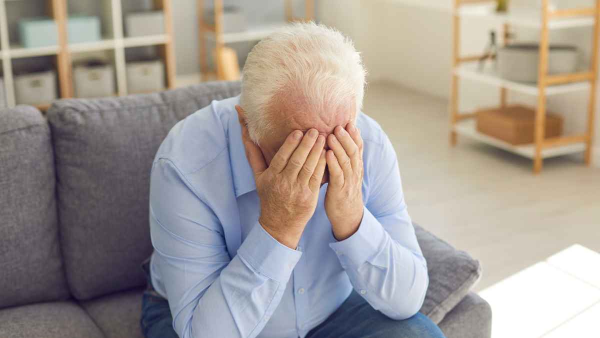 Pensionista preocupado cubriendo el rostro sentado en un sofá tras conocer devolución al SEPE