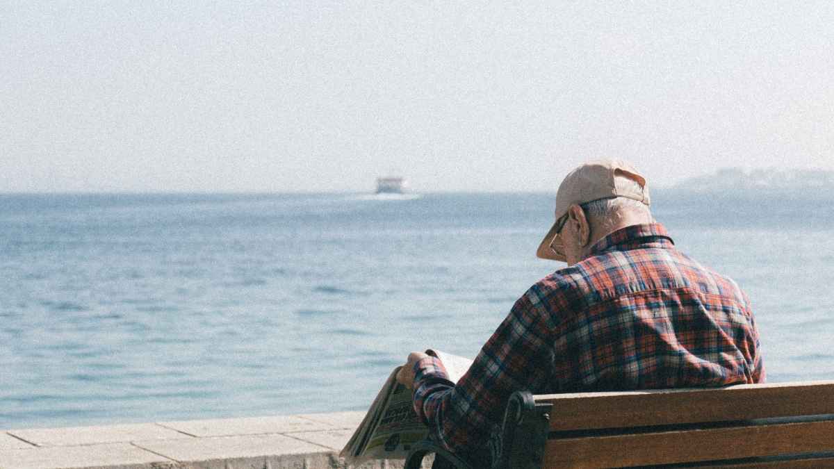Pensionista leyendo el periódico frente al mar mientras espera la paga extra de verano 2025
