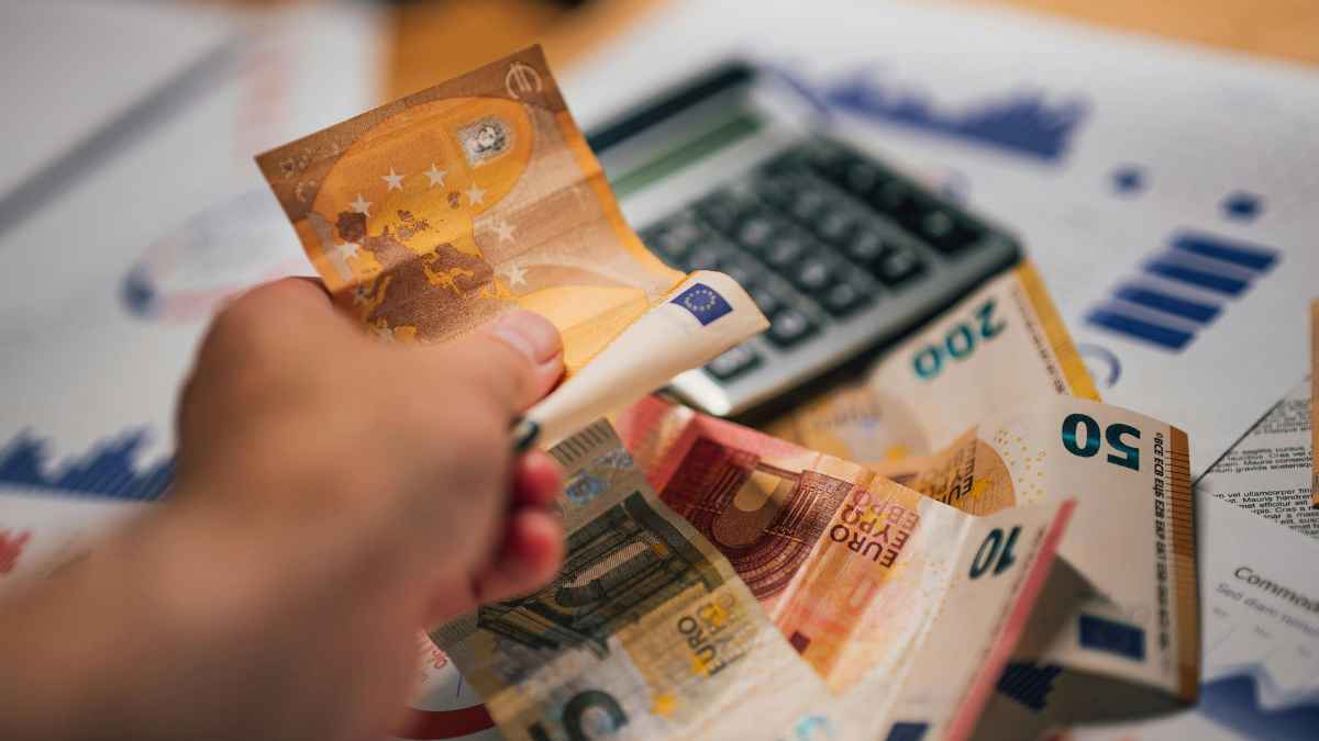 Mano contando billetes de euro junto a calculadora; ayudas SEPE para ingresos inferiores a 888 euros