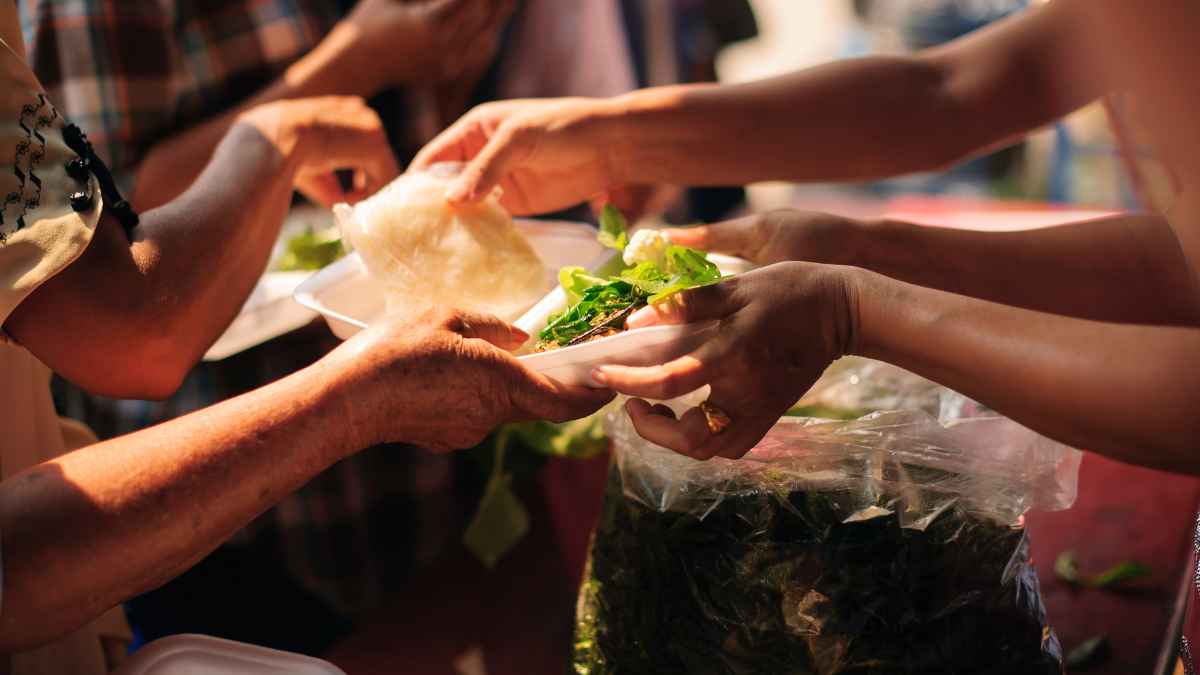 Manos repartiendo comida sobrante a personas sin hogar en el aeropuerto de Marsella