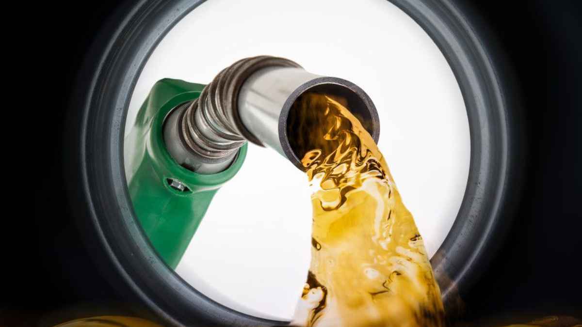 Boquilla verde de surtidor vertiendo gasolina dorada en el depósito, posible mezcla con agua