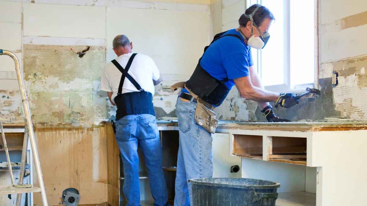 Dos hombres realizando trabajos de reforma en una cocina, uno de ellos ayudando con herramientas de obra durante una baja médica laboral.