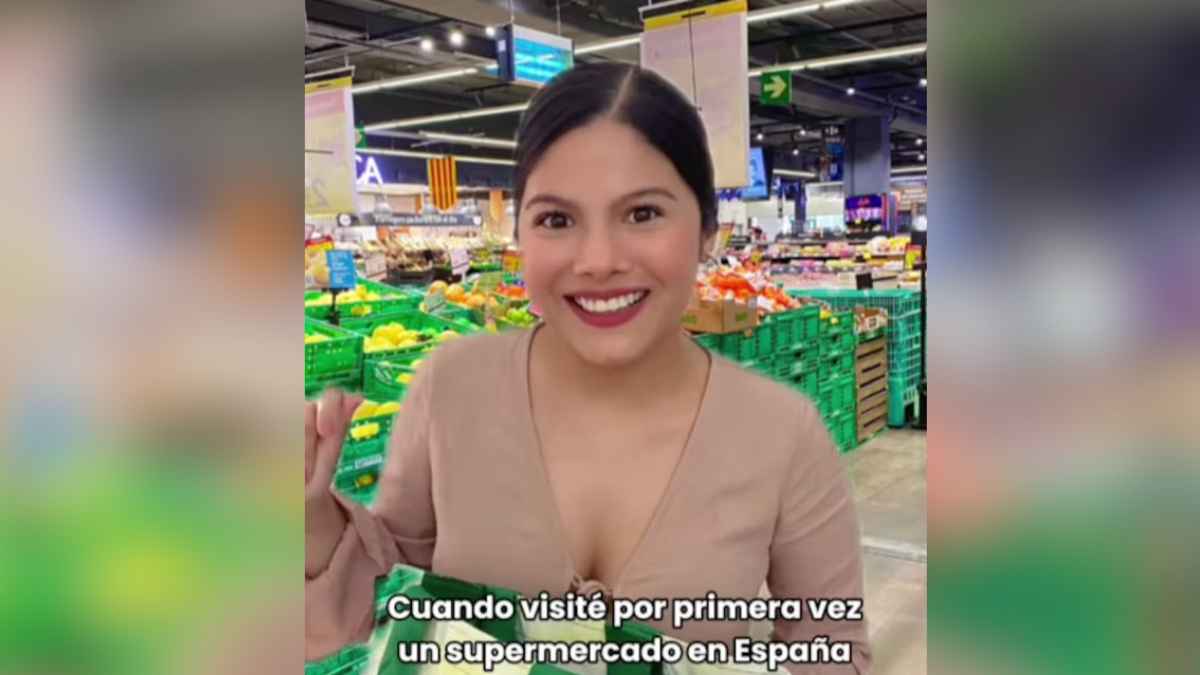 Tiktoker ecuatoriana sonríe en un supermercado en España, con cajas de fruta y verduras de fondo