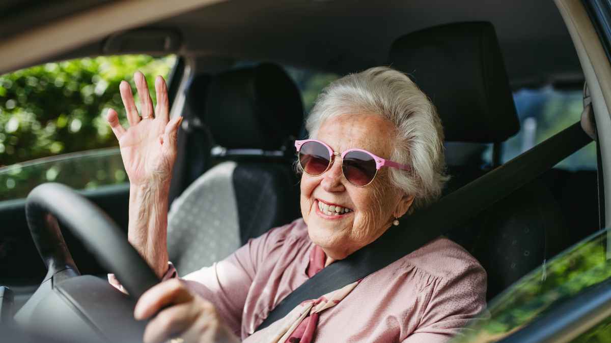 Mujer mayor conduciendo sonriente con gafas de sol en su coche