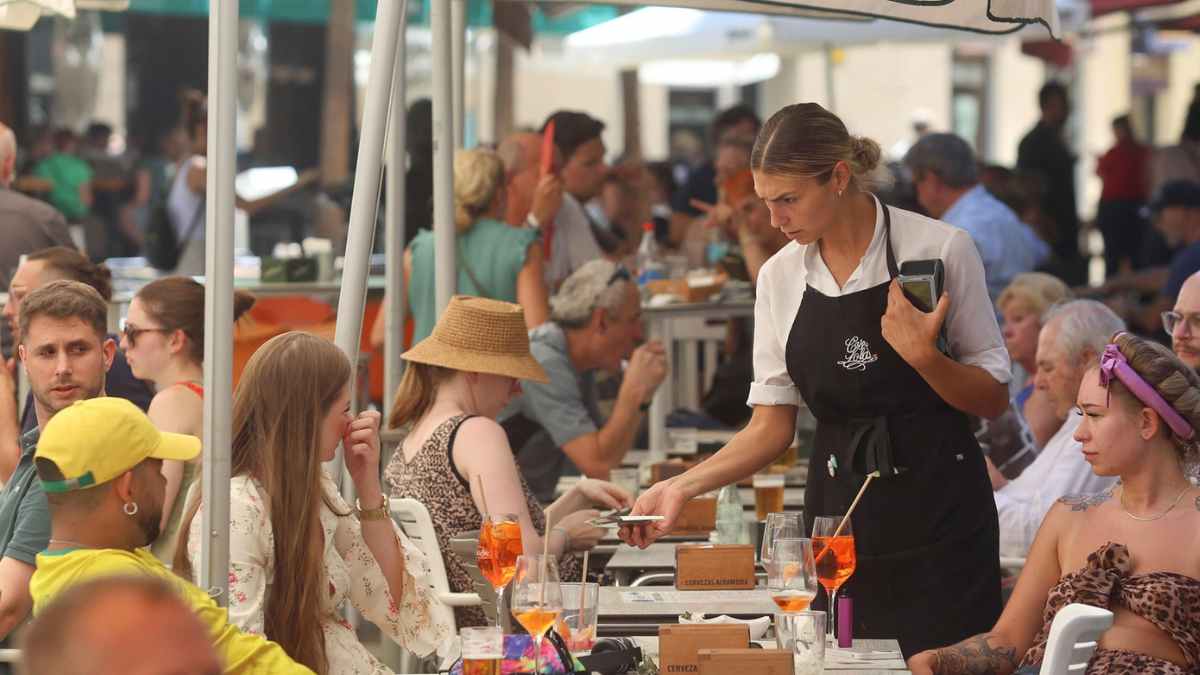 Camarera atendiendo a turistas en una terraza abarrotada, reflejo del récord de empleo en la hostelería española