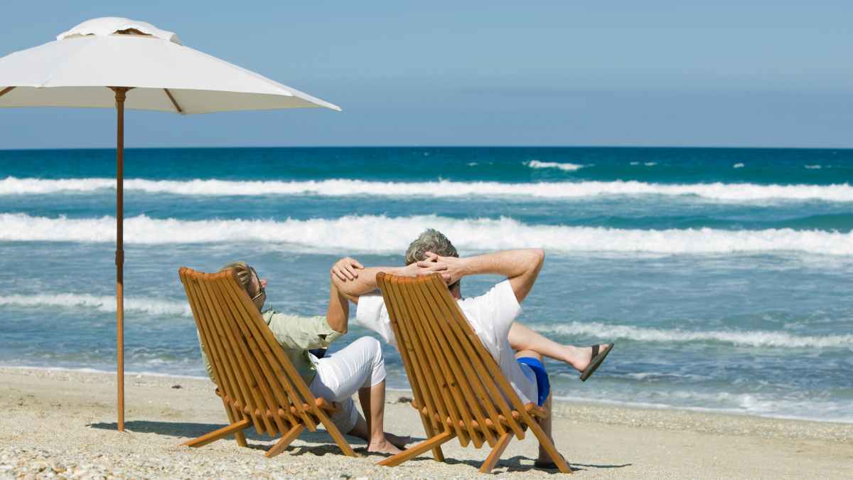 Pareja de jubilados de 65 años relajándose en la playa tras descubrir 1,3 millones sin plan de ahorros