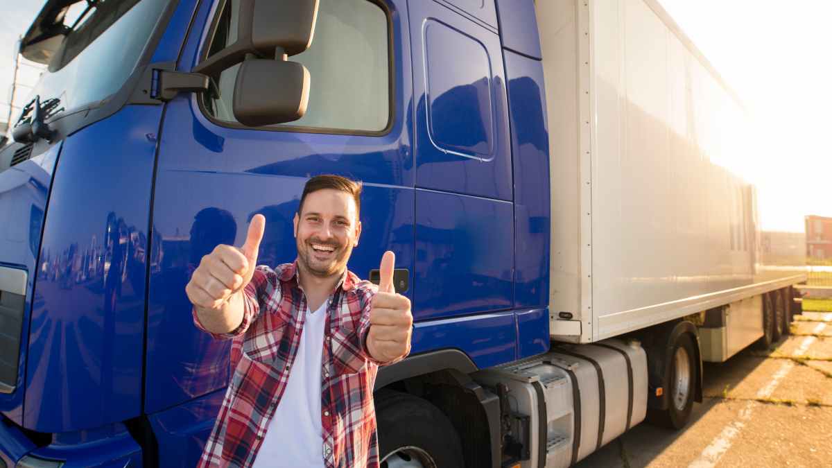 Joven camionero mostrando pulgares arriba junto a camión azul, ayudas de 2 000 euros del Ministerio de Transportes