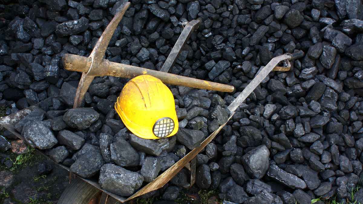 Casco de minero amarillo sobre un montón de carbón y herramientas de minería, representando el sector de la minería del carbón en España