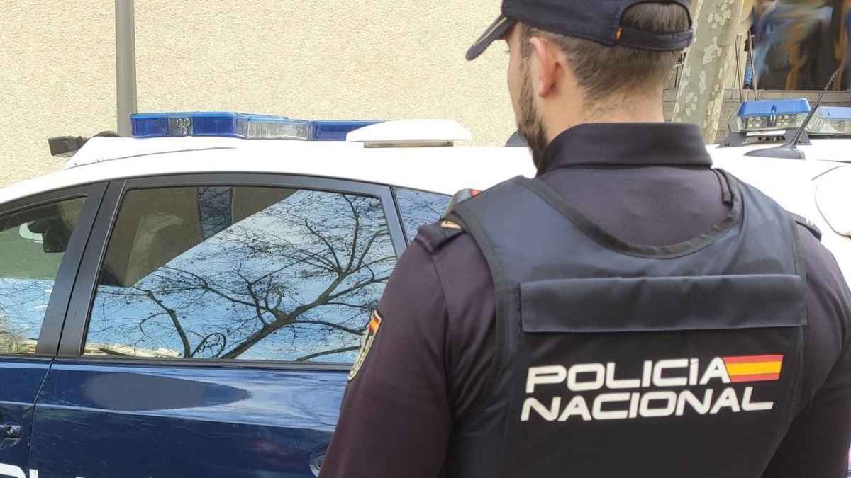 Agente de la Policía Nacional junto a un coche patrulla en la investigación por robo de joyas en una funeraria de Avilés