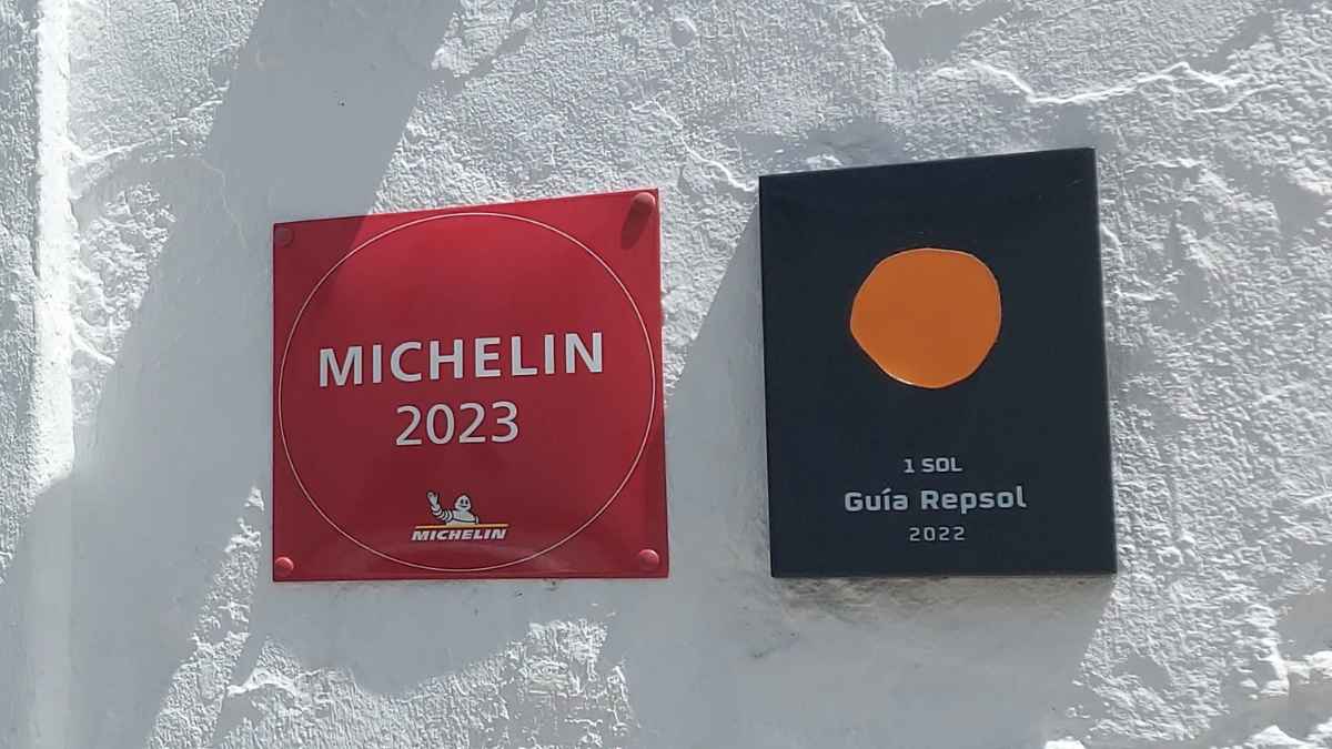 Placas oficiales del restaurante con estrella Michelin 2023 y 1 Sol Guía Repsol 2022 sobre pared blanca