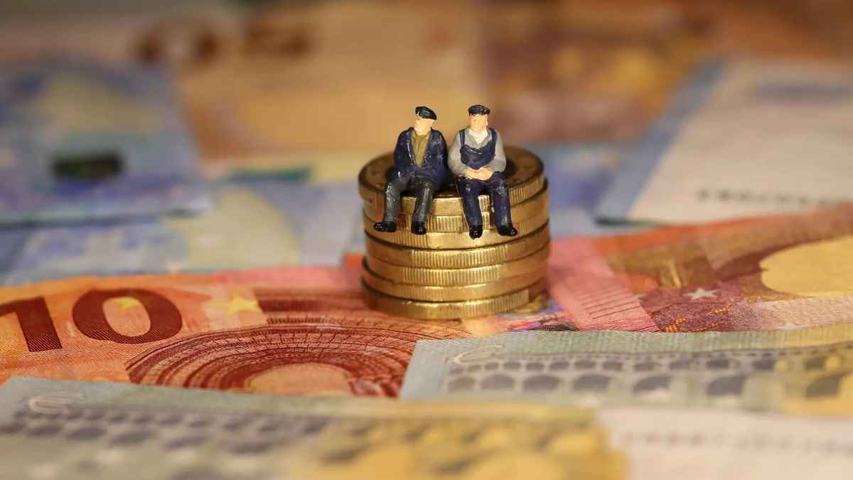 Dos figuras de pensionistas sentados sobre monedas y billetes de euro representando la pensión por cuidado de familiares