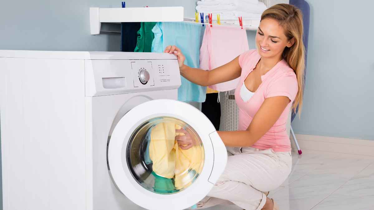 Mujer sacando ropa limpia de una lavadora con puerta abierta para evitar malos olores y gastos innecesarios de luz