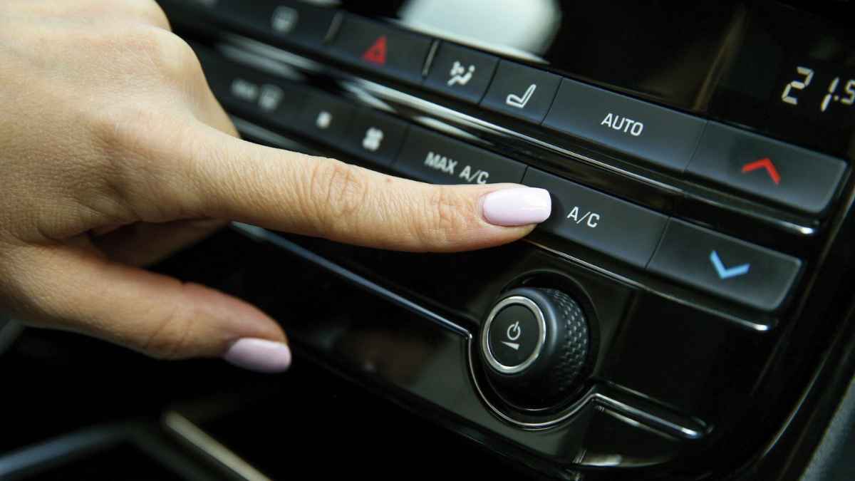 Mano apagando el aire acondicionado del coche para evitar averías y prolongar la vida útil del sistema.