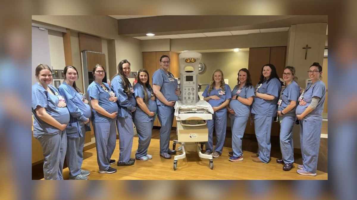 14 enfermeras embarazadas del hospital materno St Vincent de Green Bay posan con sus uniformes azules junto a una cuna térmica en la unidad Women and Infants