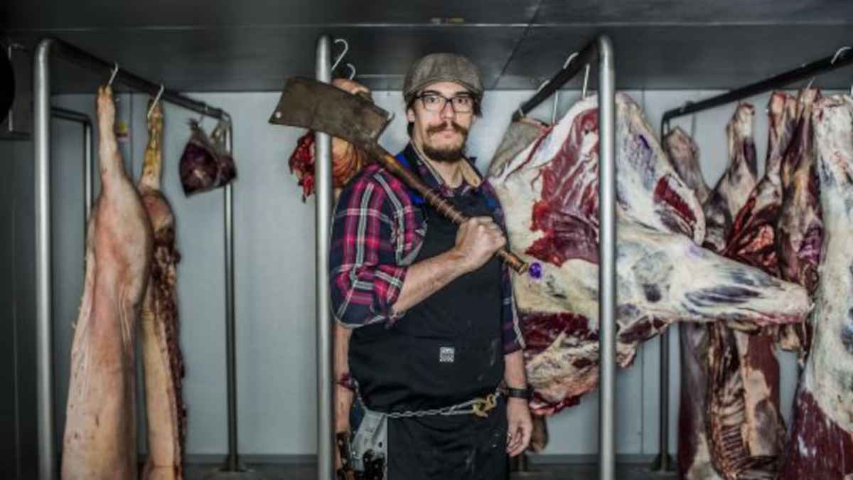Carnicero con cuchillo en una carnicería, enfrentando la escasez de mano de obra cualificada en Australia.