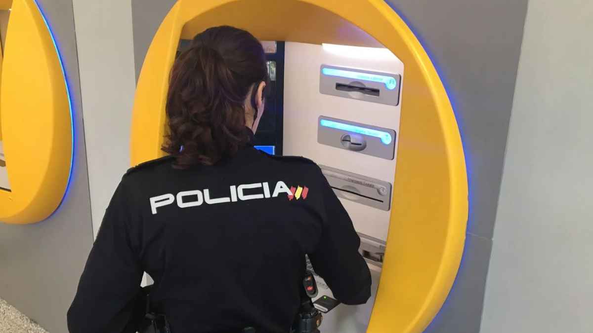 Agente de Policía Nacional inspeccionando cajero automático en la calle para prevenir clonación de tarjetas bancarias