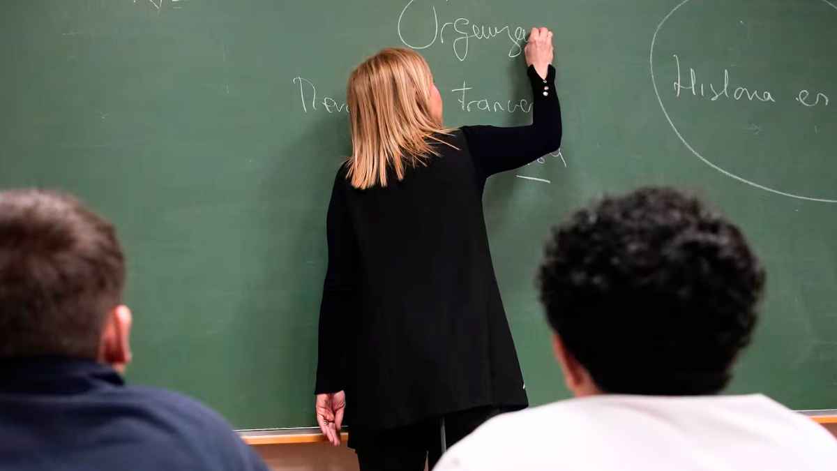 Profesora escribiendo en la pizarra durante una clase, vista desde la perspectiva de los alumnos