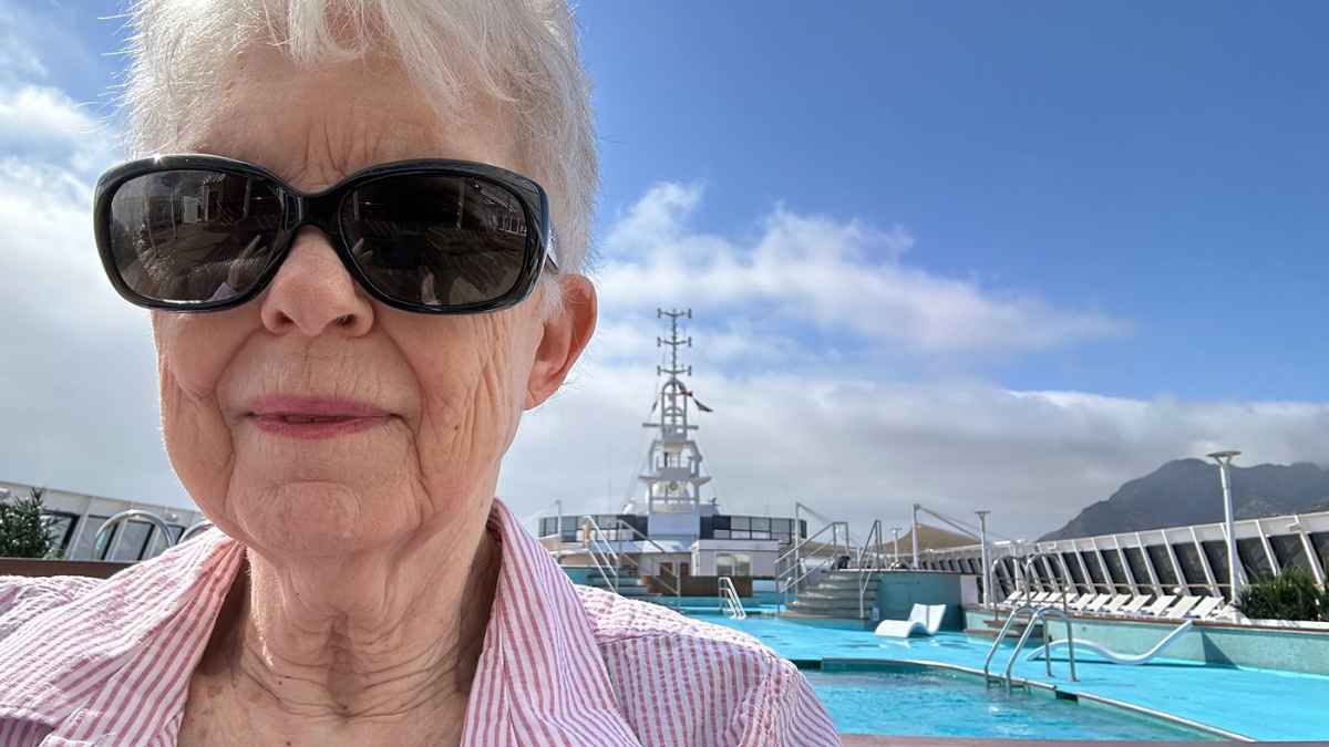 Anciana de 77 años en la cubierta de un crucero con piscina y cielo despejado
