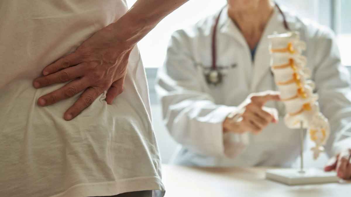 Paciente con dolor lumbar en consulta; médico señala columna vertebral, ejemplo de baja médica tras la reforma del Estatuto de los Trabajadores.