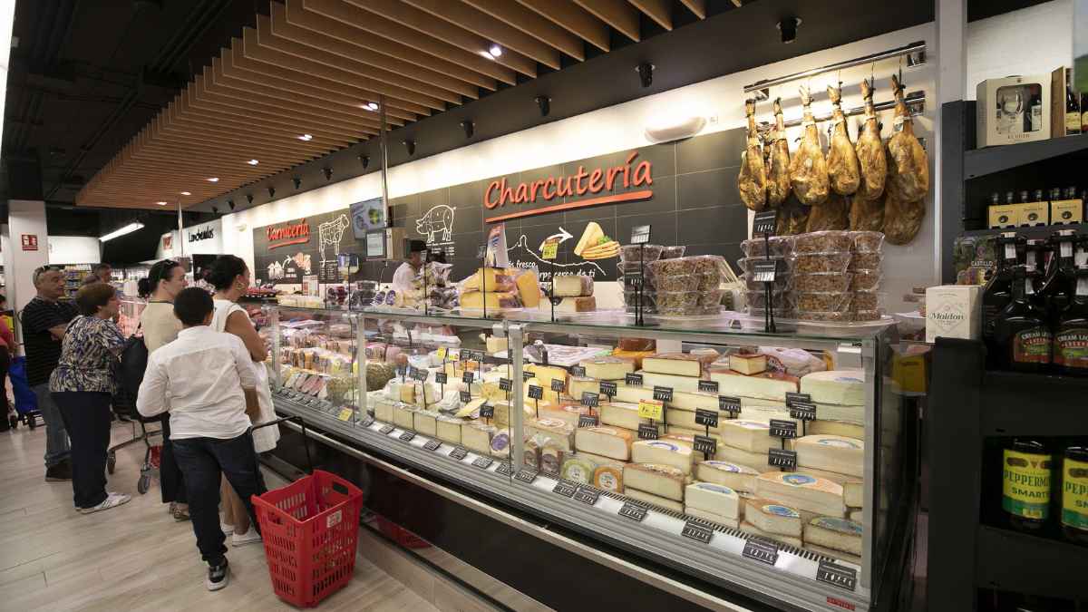 Mostrador de charcutería de Carrefour con variedad de quesos y clientes en fila ante el dependiente.
