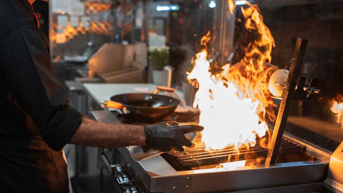 Cocinero trabajando en cocina con llamas en la parrilla
