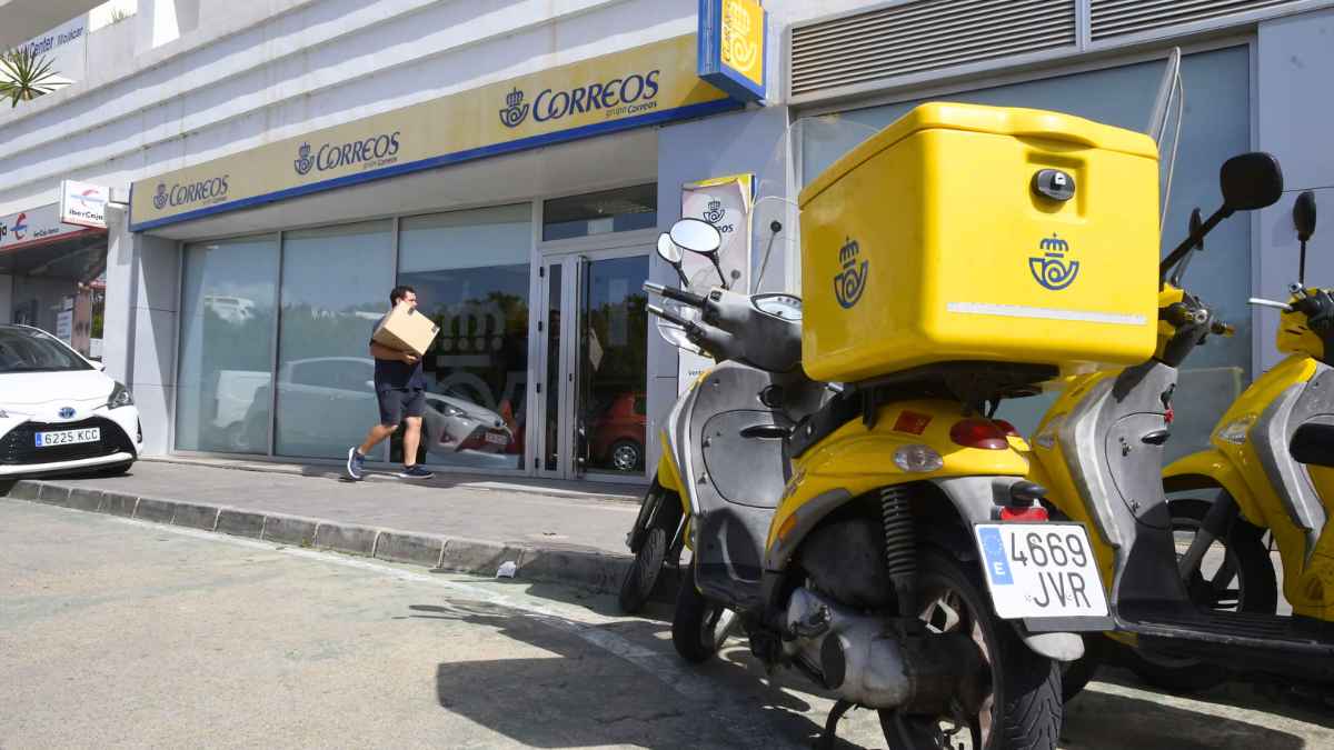 Oficina de Correos con repartidor y motos estacionadas frente a la entrada