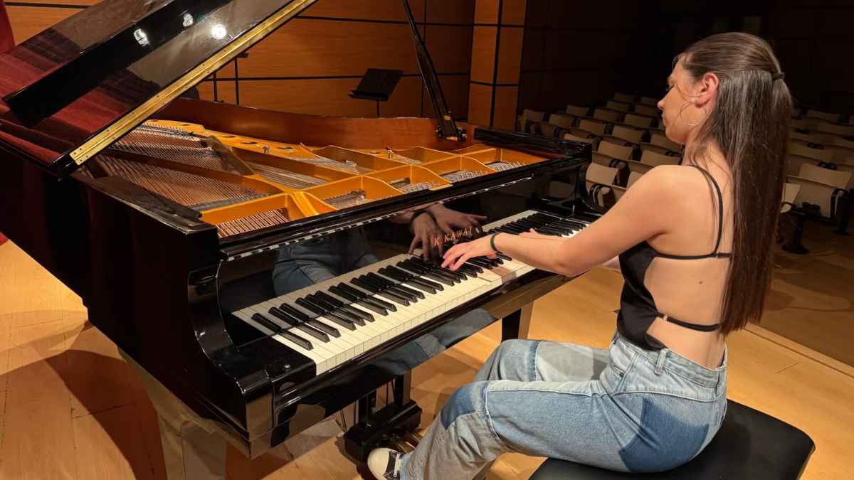Joven pianista tocando un piano de cola en auditorio vacío, becas de 10.000 € para estudios de música y artes escénicas.