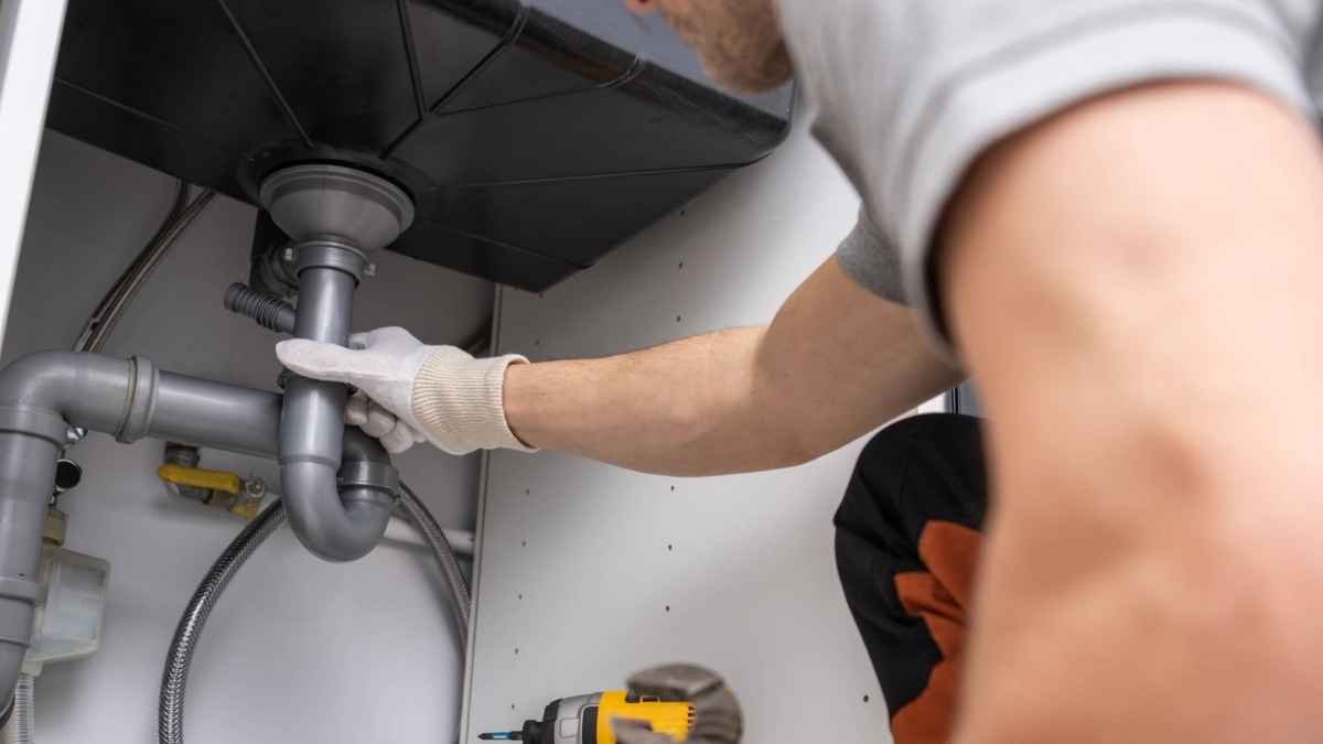 Fontanero revisando tuberías bajo el fregadero con guantes de trabajo