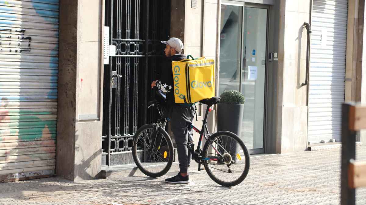 Repartidor de Glovo en bicicleta frente a un portal en Sevilla.