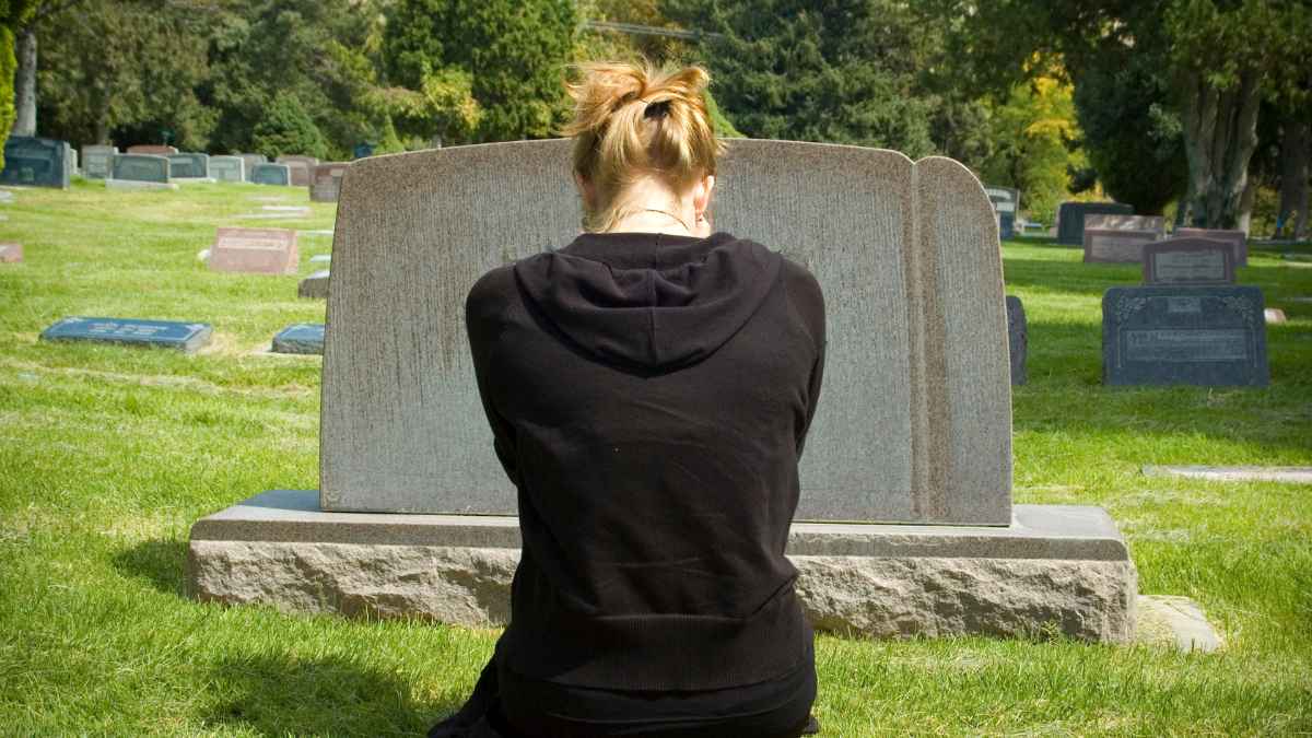 Mujer frente a la tumba de su madre en un cementerio tras fraude con pensión de viudedad descubierto por la Seguridad Social