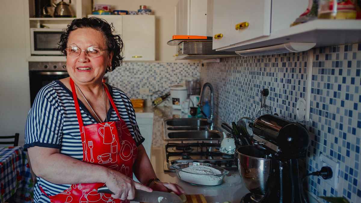 Mujer jubilada de 74 años sonríe en la cocina mientras prepara comida en su nuevo hogar compartido