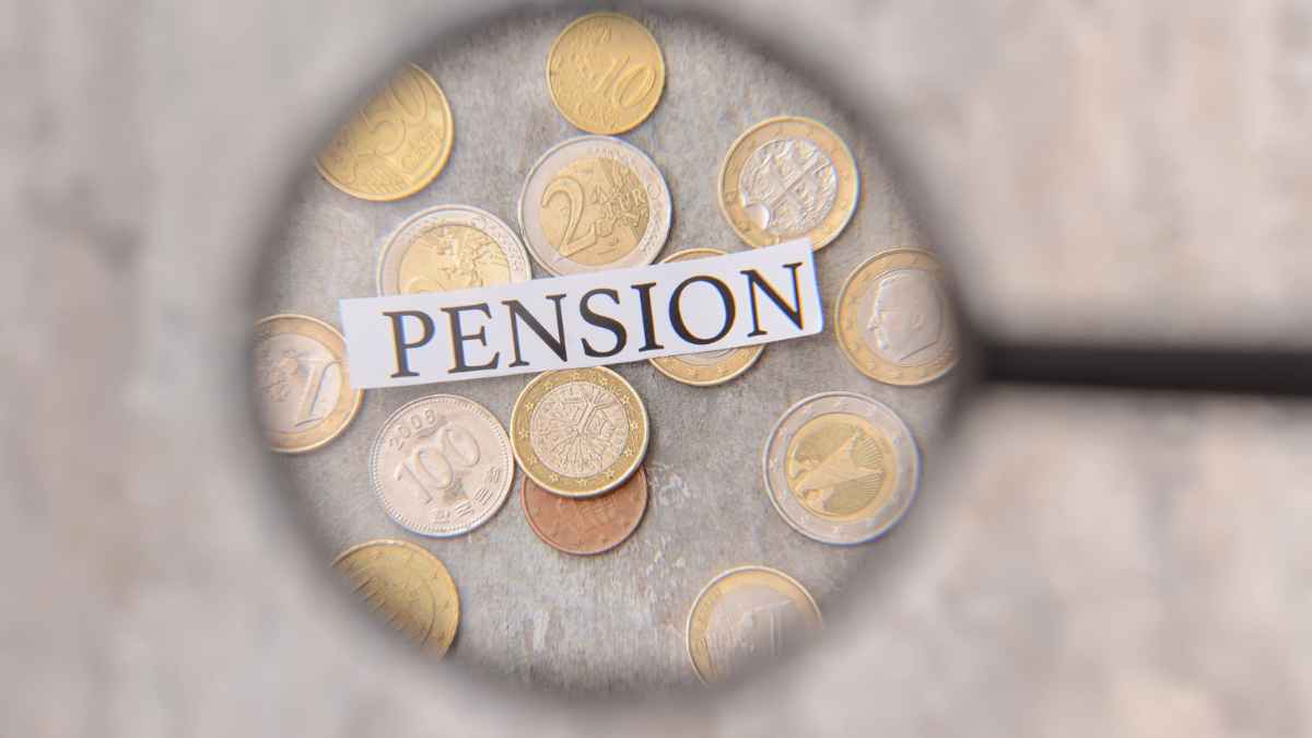 Lupa enfocando la palabra pensión sobre monedas, pensiones contributivas y no contributivas
