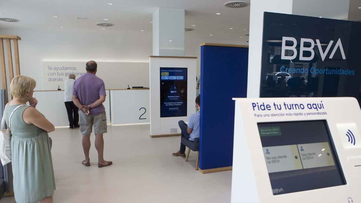 Personas esperando turno en una oficina del BBVA para operaciones bancarias en efectivo