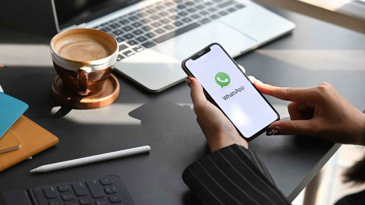 Persona usando WhatsApp en el móvil en un escritorio de trabajo con café y portátil